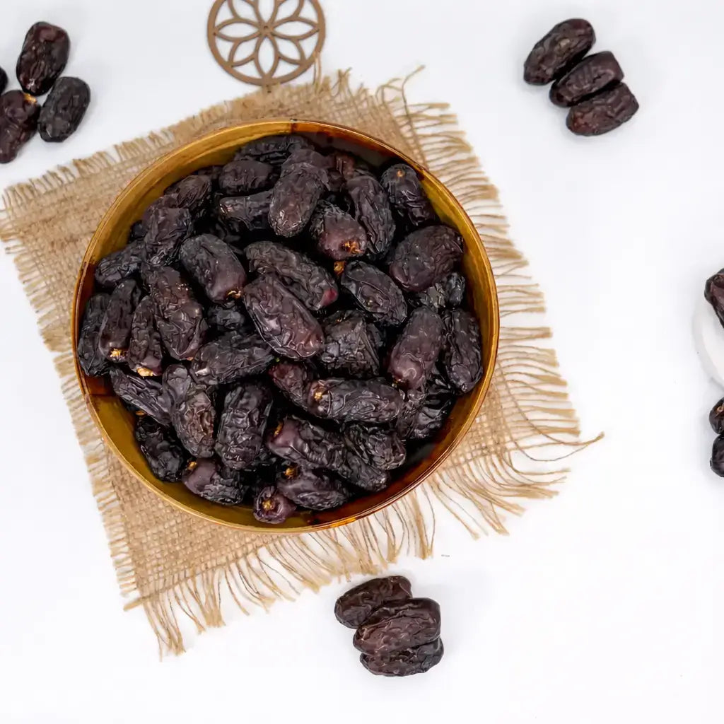 Bowl of dark dried fruits on a textured mat with scattered fruits around.
