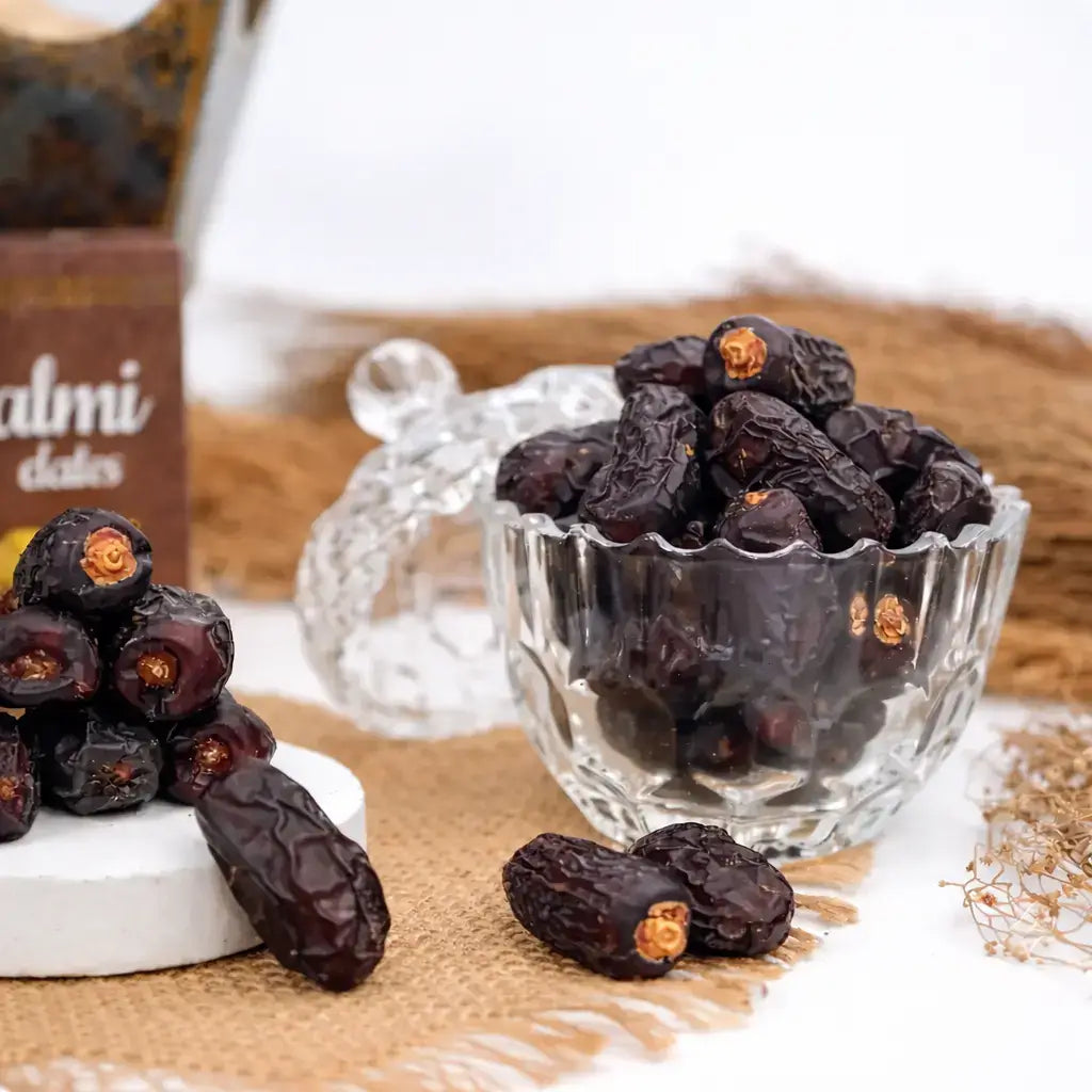Dried dates in a glass bowl and on a surface with a box labeled 'Almi Dates' in the background.