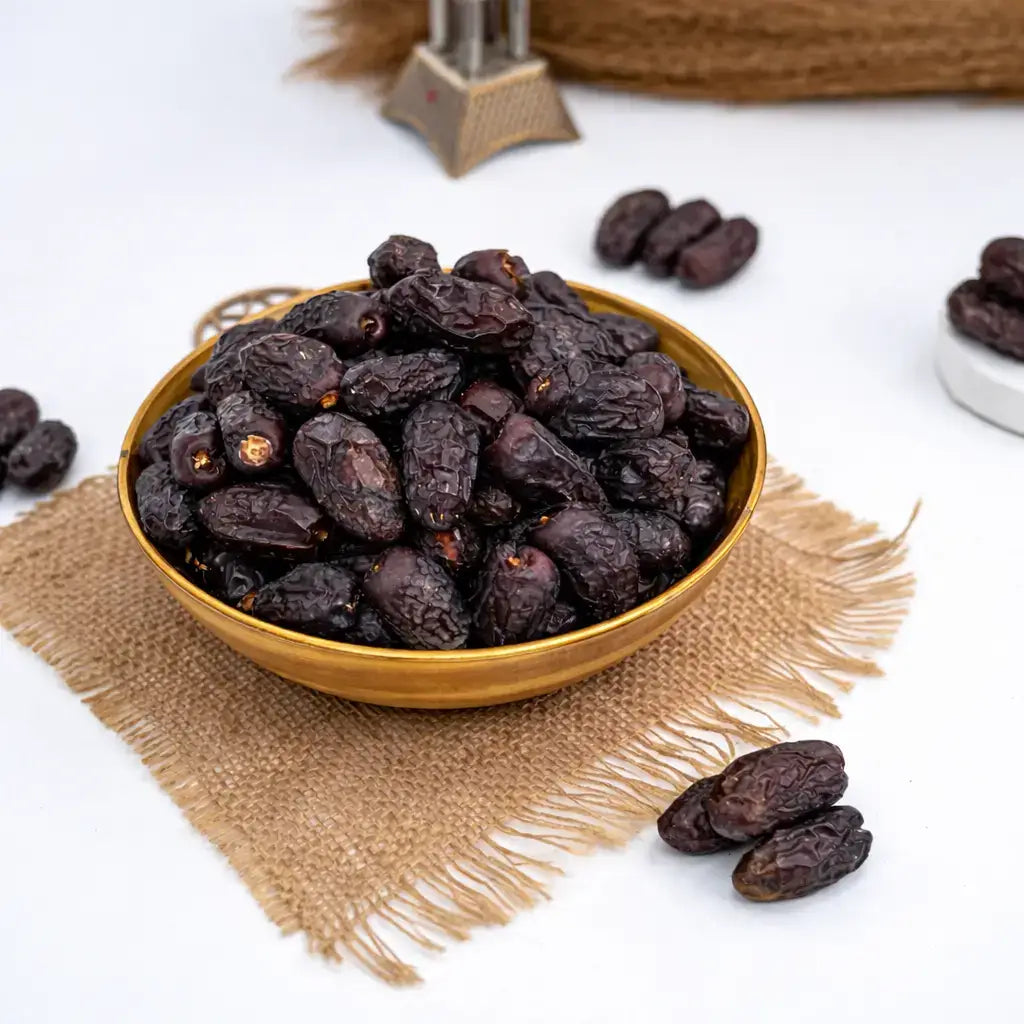 Gold bowl filled with dark raisins on a textured beige mat with scattered raisins.