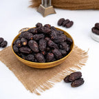 Gold bowl filled with dark raisins on a textured beige mat with scattered raisins.
